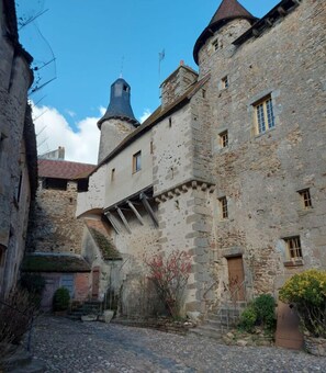 A historic stone building with a tower, narrow cobblestone street, and a small garden area.