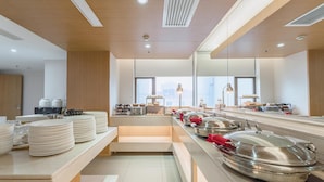 A modern hotel kitchen with buffet-style service, including stacked plates and covered food stations.