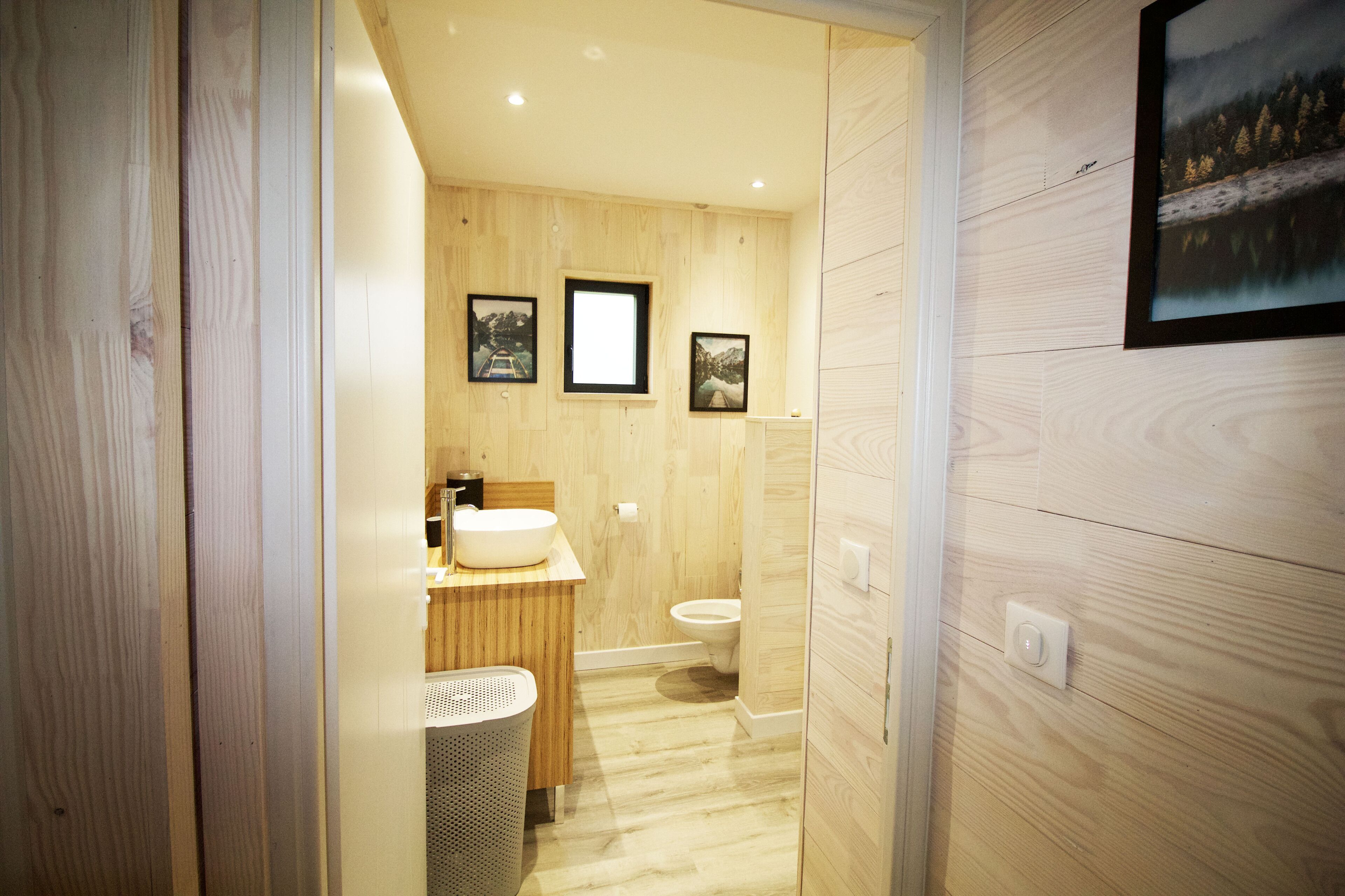 Une salle de bain moderne avec un lambris en bois, un lavabo, des toilettes et des tableaux encadrés accrochés au mur.