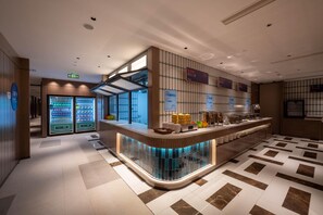 A modern hotel lobby with a curved reception desk, vending machines, and a tiled floor.