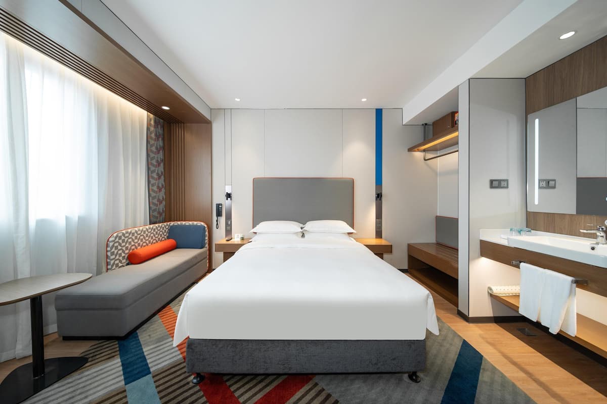 Une chambre d’hôtel comprenant un lit, un canapé, un bureau, une salle de bain avec un lavabo et un miroir, et une fenêtre avec des rideaux.