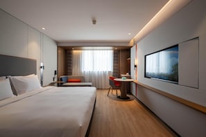 Habitación de hotel con una cama grande, un escritorio con silla, televisor y ventana con cortinas.