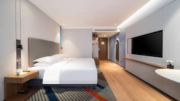 Quarto de hotel moderno com cama, mesa de cabeceira, televisão e um espelho grande.