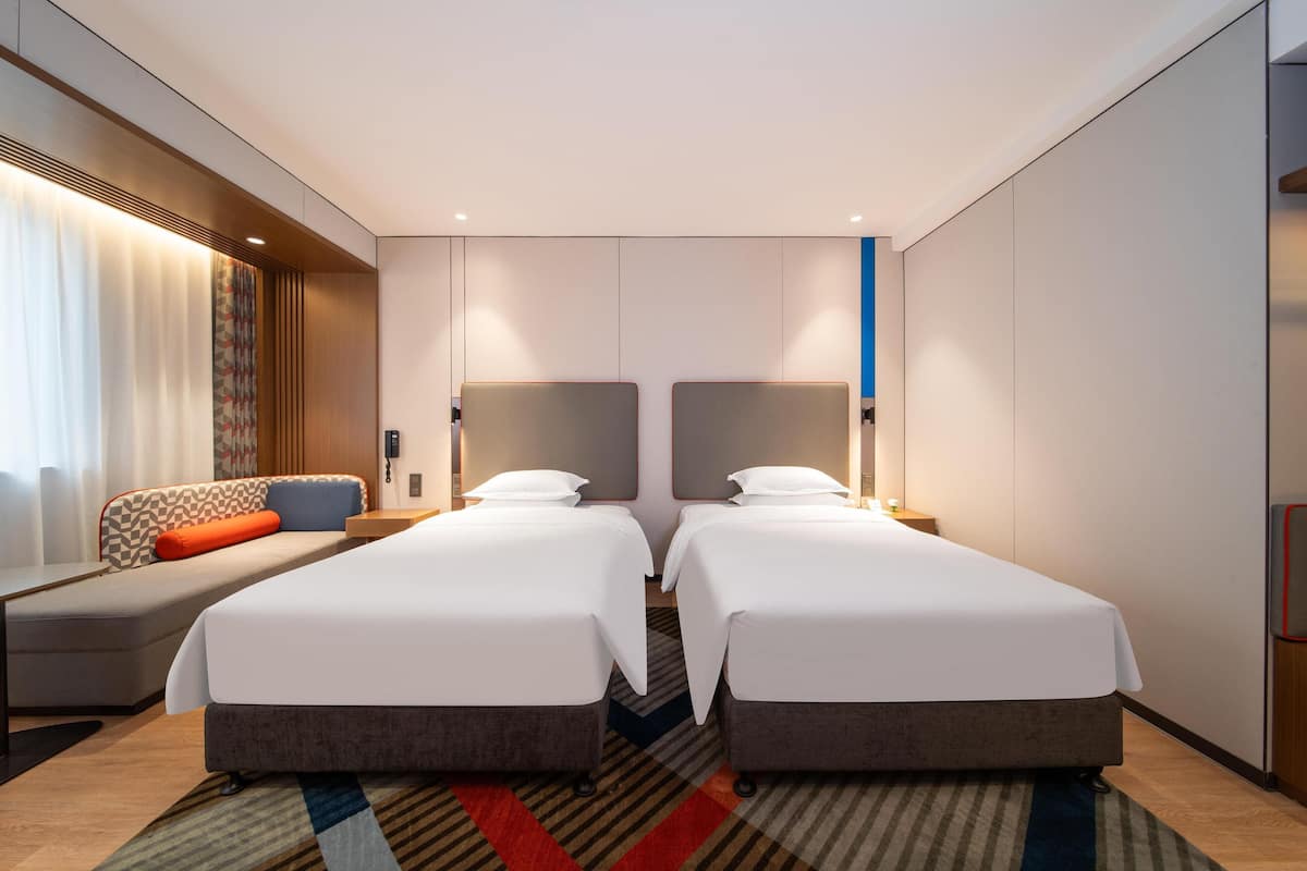 Une chambre d’hôtel avec deux lits, un canapé, un bureau et un grand miroir.