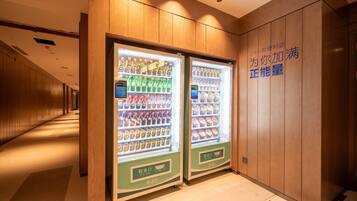 Um corredor com duas máquinas de venda automática repletas de bebidas e lanches, painéis de madeira nas paredes e uma placa com caracteres chineses.