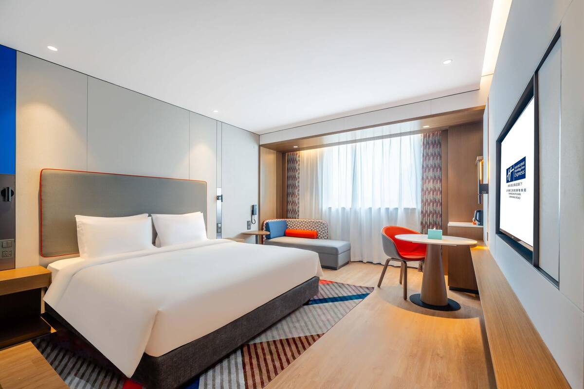 Une chambre d’hôtel moderne équipée d’un grand lit, d’un bureau, d’une chaise et d’un écran de télévision.