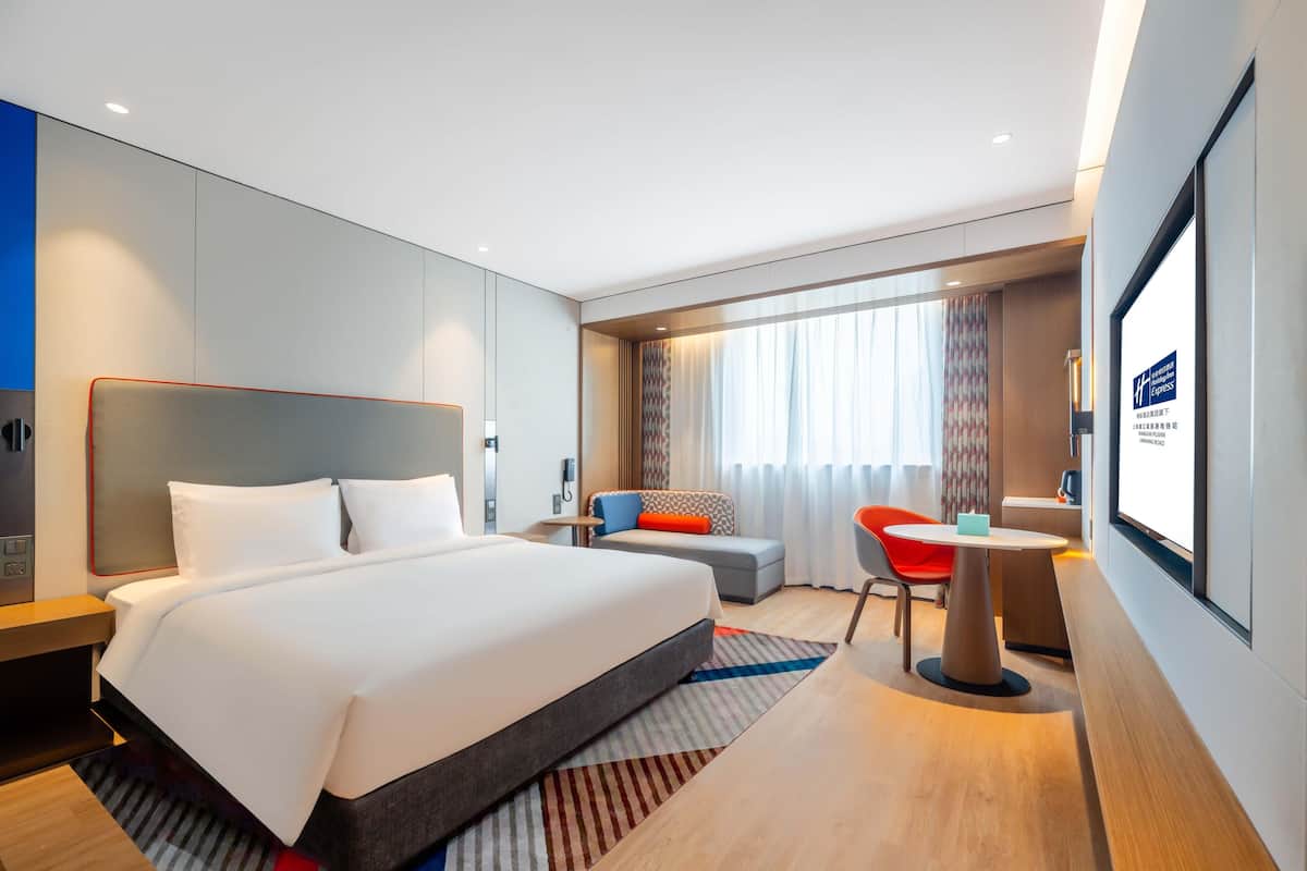 A modern hotel room with a large bed, a desk, a chair, and a TV screen.