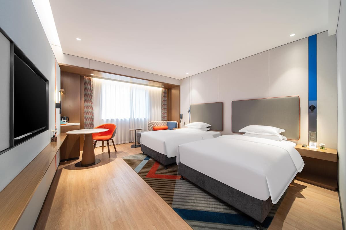 Une chambre d’hôtel avec deux lits, une télévision, un bureau et une fenêtre avec des rideaux.