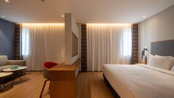 Quarto de hotel com cama, escrivaninha, cadeira, sofá e televisão.