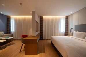 A hotel room with a bed, a desk, a chair, a sofa, and a TV.