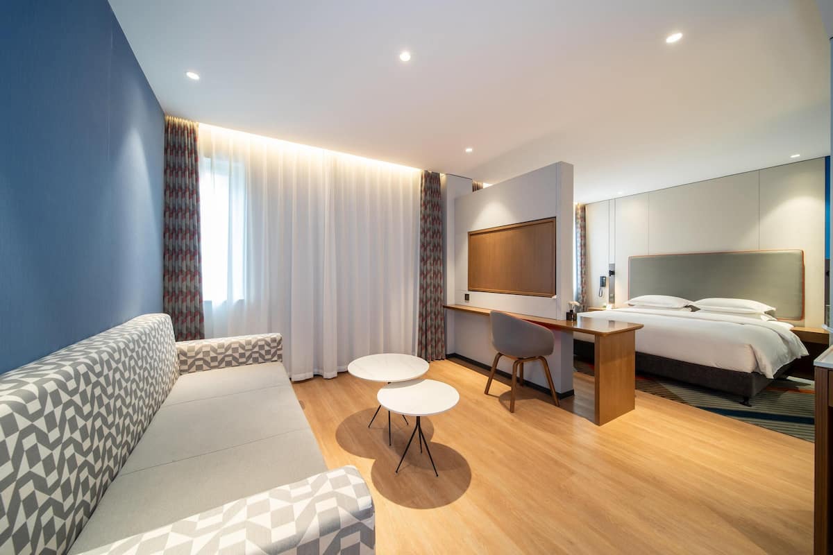 Une chambre d’hôtel moderne équipée d’un canapé, de deux petites tables rondes, d’un lit, d’un bureau et d’une télévision.