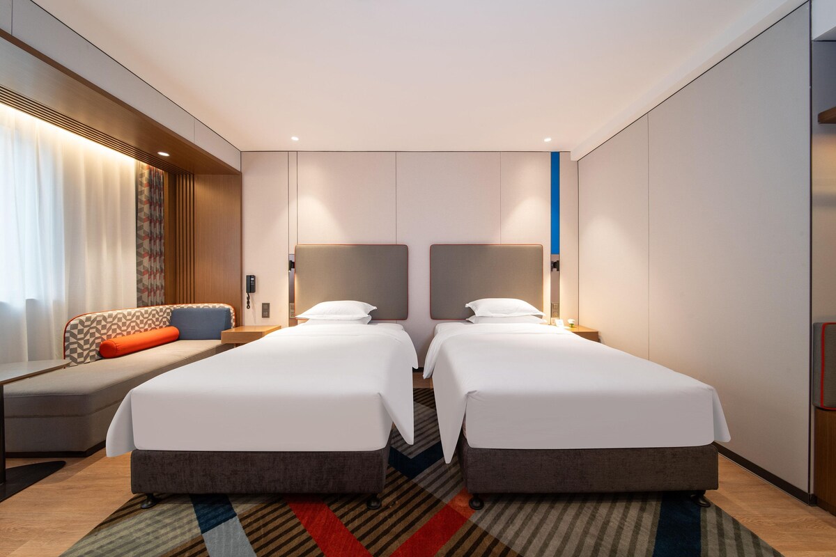 Habitación de hotel con dos camas, un sofá, un escritorio y un espejo grande.