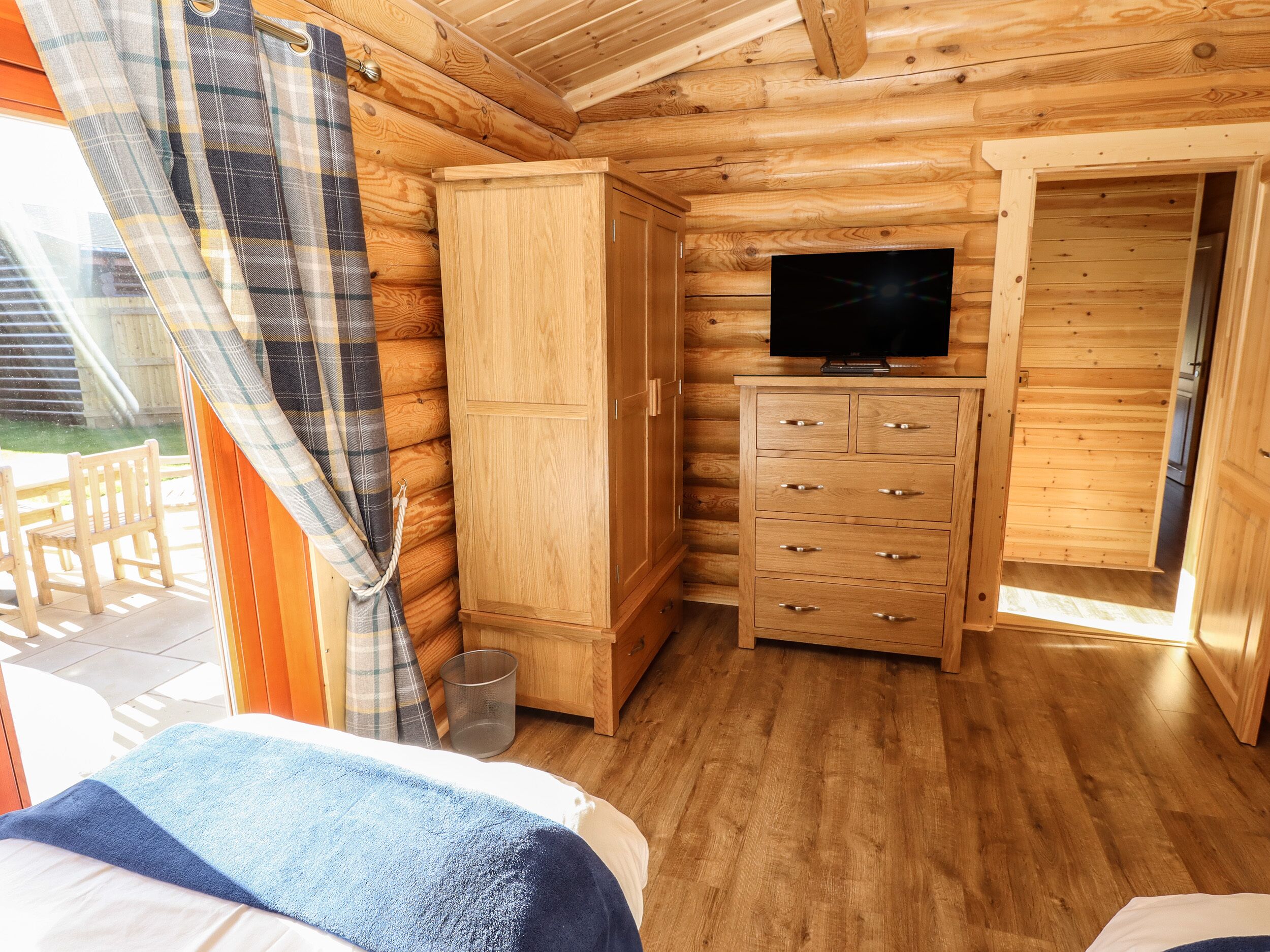 A wooden cabin room with a bed, a TV on a wooden cabinet, and a window with curtains.