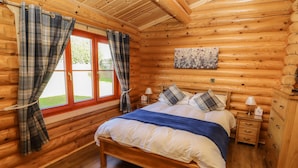 A wooden cabin bedroom with a bed, two bedside tables, and plaid curtains. - Pine Lodge (Oakham)