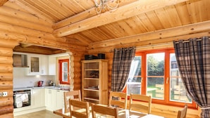 A wooden cabin interior with a dining area, kitchen, and a view of the garden. - Pine Lodge (Oakham)
