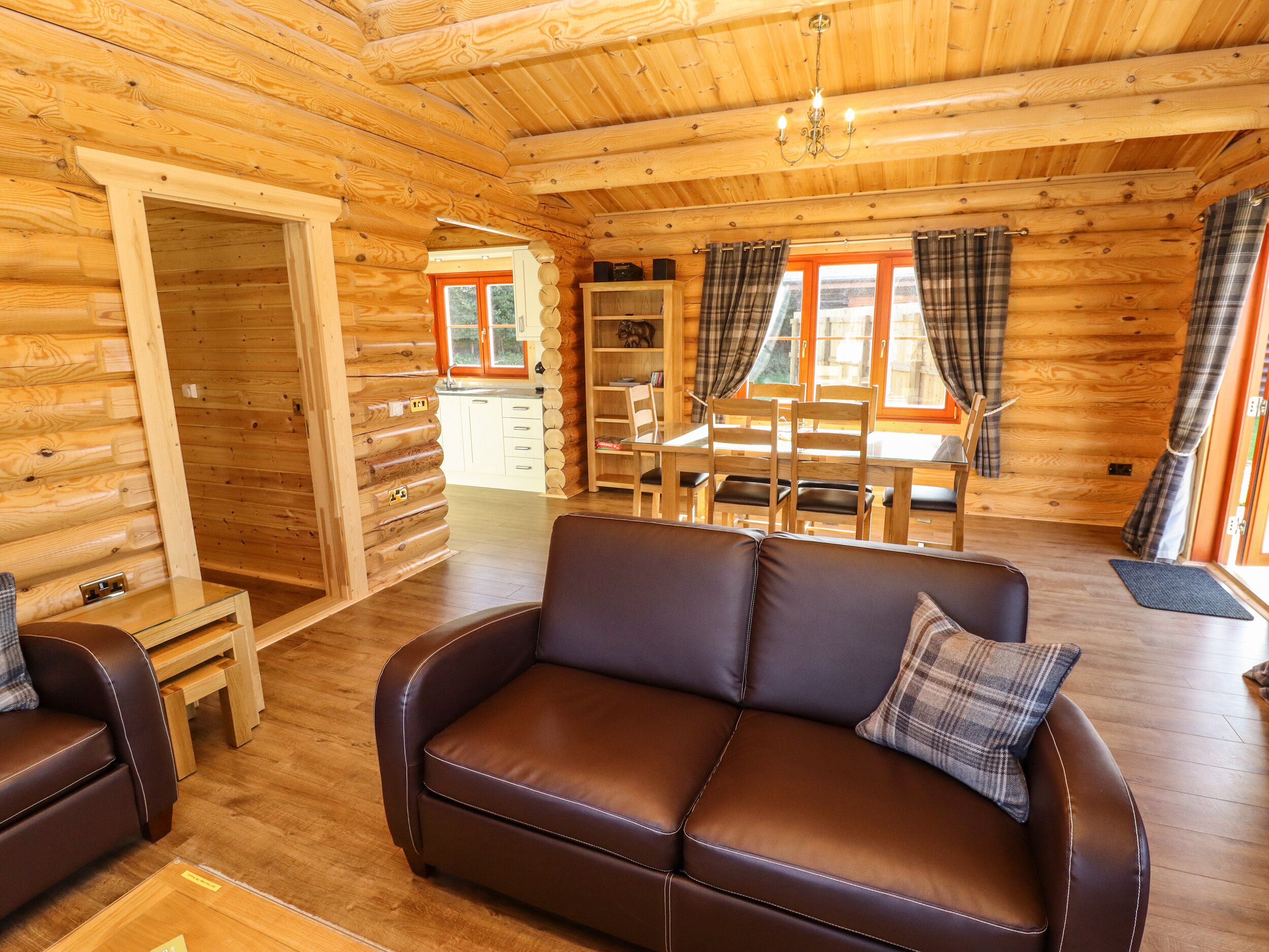 A log cabin interior with a leather sofa, dining table, chairs, and a kitchen area.