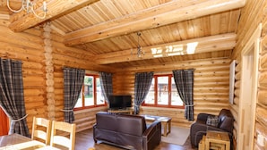 A log cabin interior with a sofa, chairs, a TV, and a dining table. - Pine Lodge (Oakham)