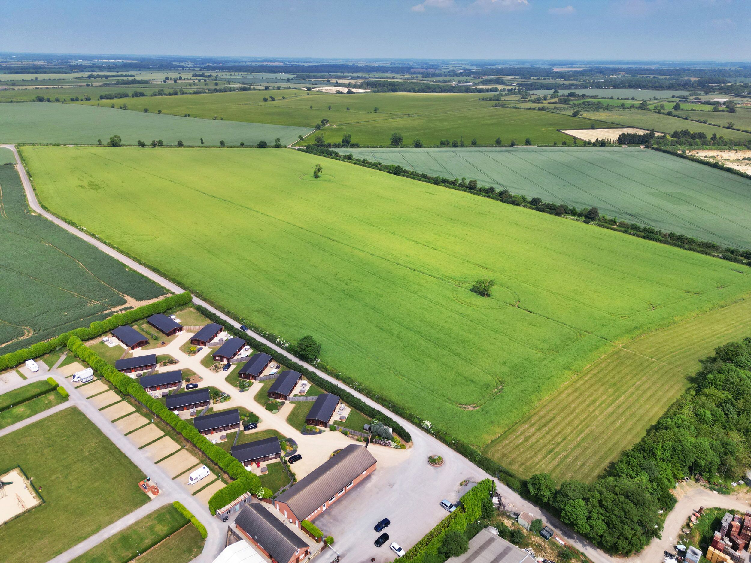 An aerial view of a rural property with multiple buildings, including a large barn and several smaller structures, surrounded by expansive green fields.
