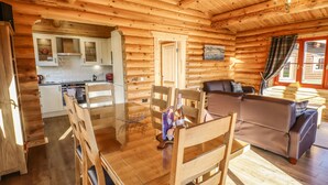A wooden cabin interior with a dining area, kitchen, and living room. - Holly Lodge (Oakham)