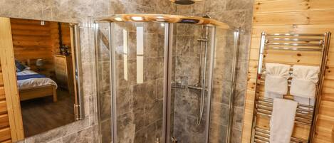 A wooden cabin bathroom with a glass-enclosed shower, a sink, and a towel rack.