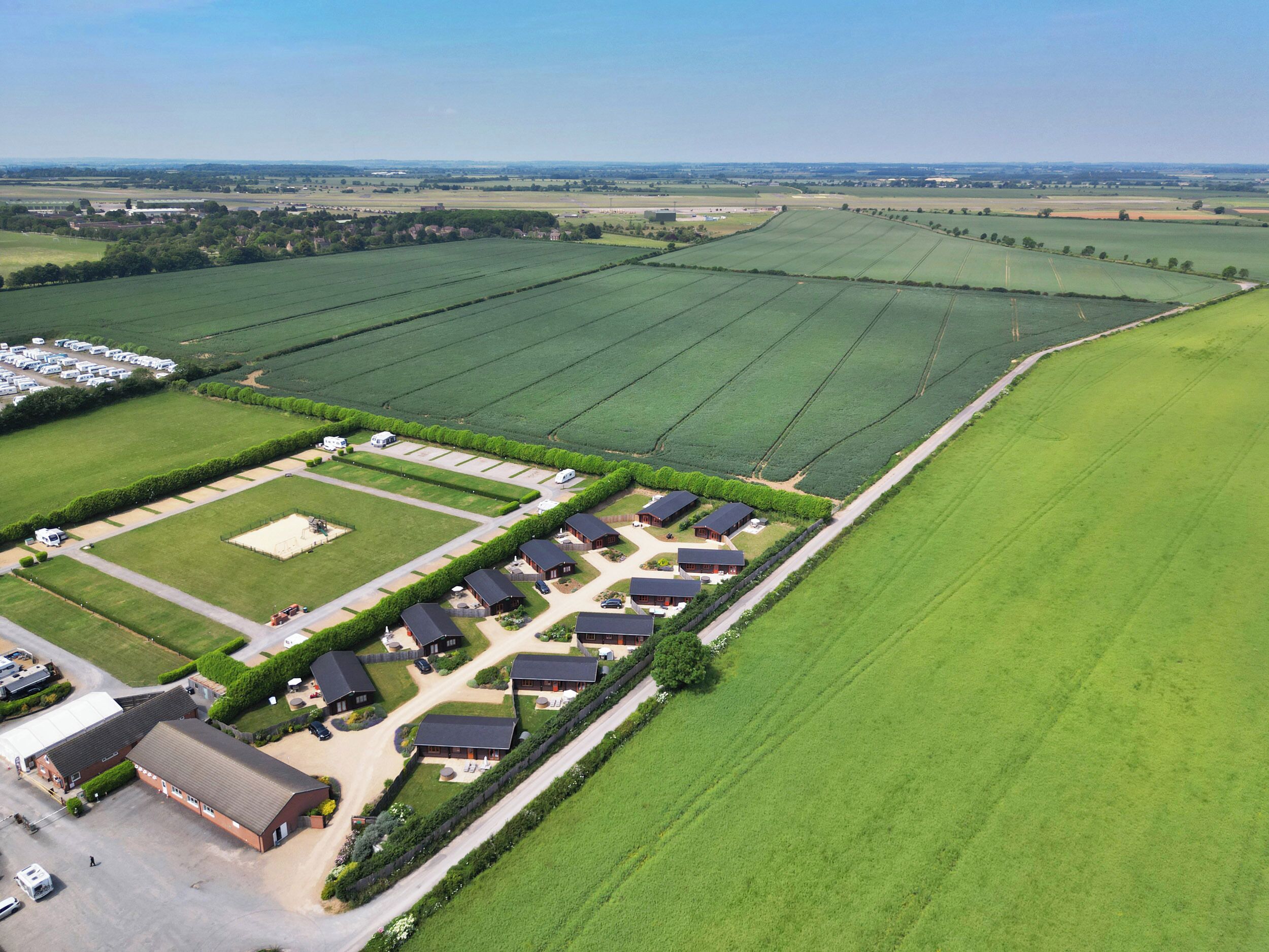 Vue aérienne d’une propriété rurale comprenant plusieurs bâtiments agricoles, un espace de stationnement et de vastes champs verdoyants.