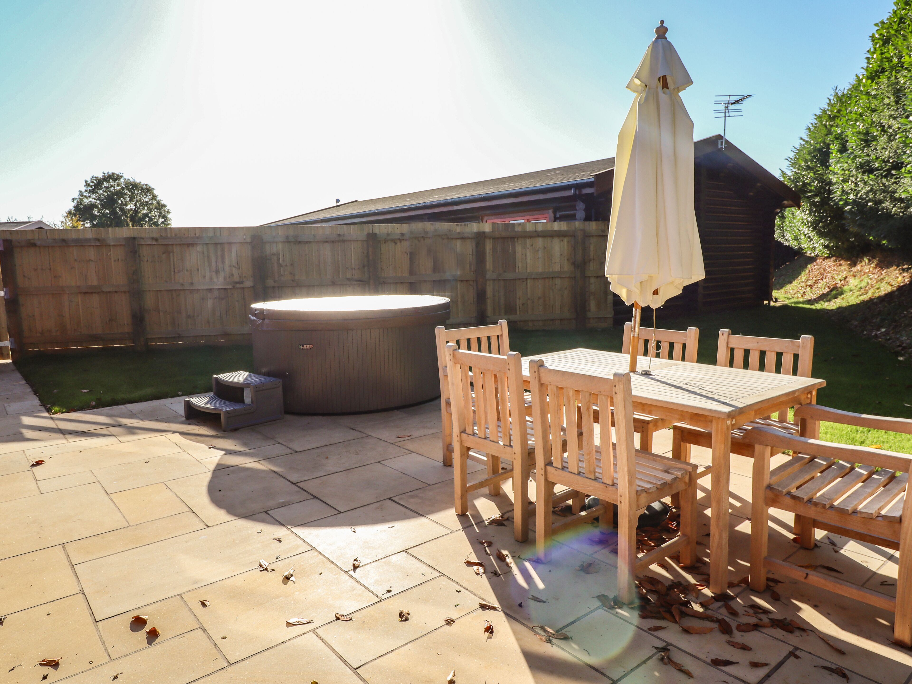A patio with a hot tub, wooden table and chairs, and a covered umbrella.
