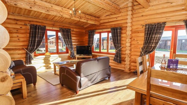 A log cabin with a wooden interior, a sofa, a television, and a dining table. - Holly Lodge (Oakham)