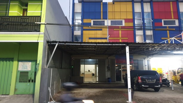 A multi-story building with a green and blue facade, a covered entrance, and a parked black SUV. - OYO 3508 Griya Aisyah Karah Syariah (Surabaya)