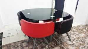 A round glass table with two chairs, one red and one black, in a room with tiled flooring and a white door in the background. - OYO 3508 Griya Aisyah Karah Syariah (Surabaya)