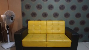 A yellow leather sofa against a patterned wallpaper, with a standing fan beside it. - OYO 3508 Griya Aisyah Karah Syariah (Surabaya)