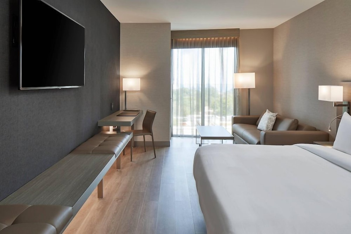 A hotel room with a bed, a desk, a chair, a sofa, and a TV.