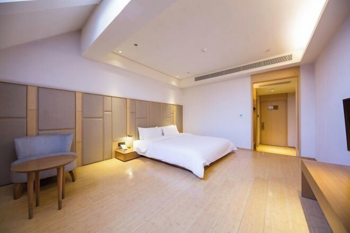 A modern hotel room with a large bed, a seating area, and a walk-in closet.