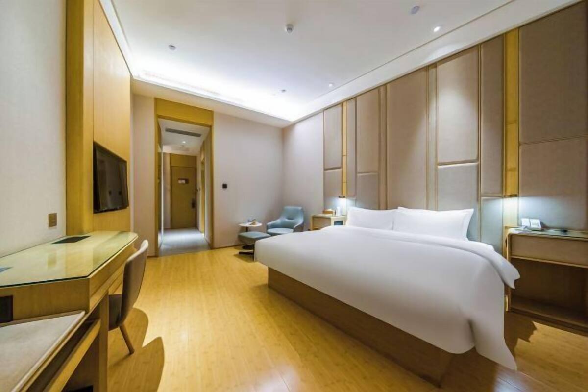 A hotel room with a large bed, a desk, a chair, a TV, and a bedside table.