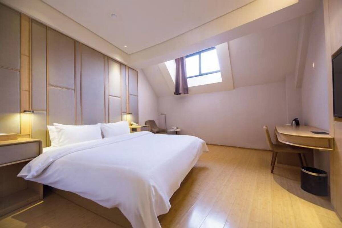 A bedroom with a bed, a desk, a chair, a window, and a TV.