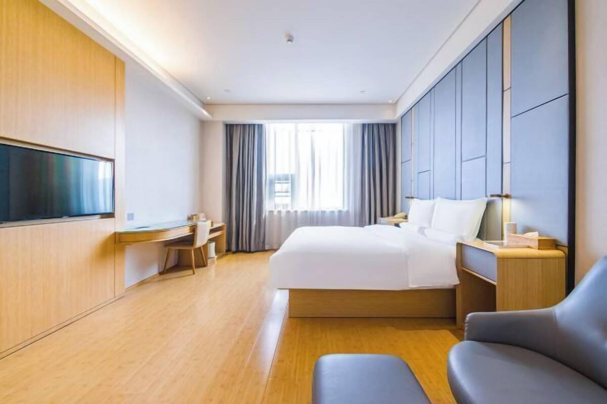 A hotel room with a bed, desk, chair, TV, and a large window with curtains.
