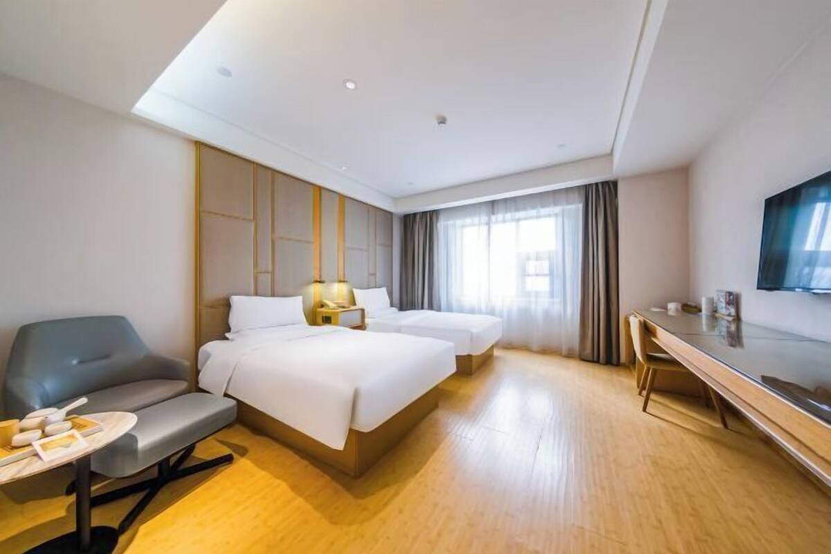 A hotel room with two beds, a desk, a chair, a sofa, and a TV.