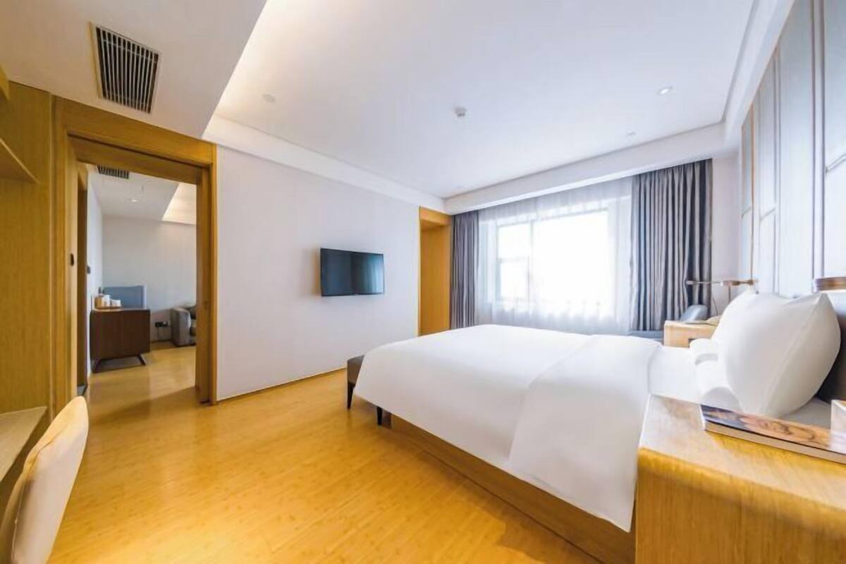 A hotel room with a large bed, a flat-screen TV, a bedside table, and a window with curtains.