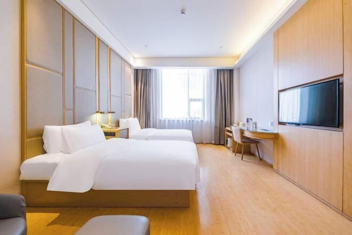 A hotel room with two beds, a desk, a TV, and a window with curtains.