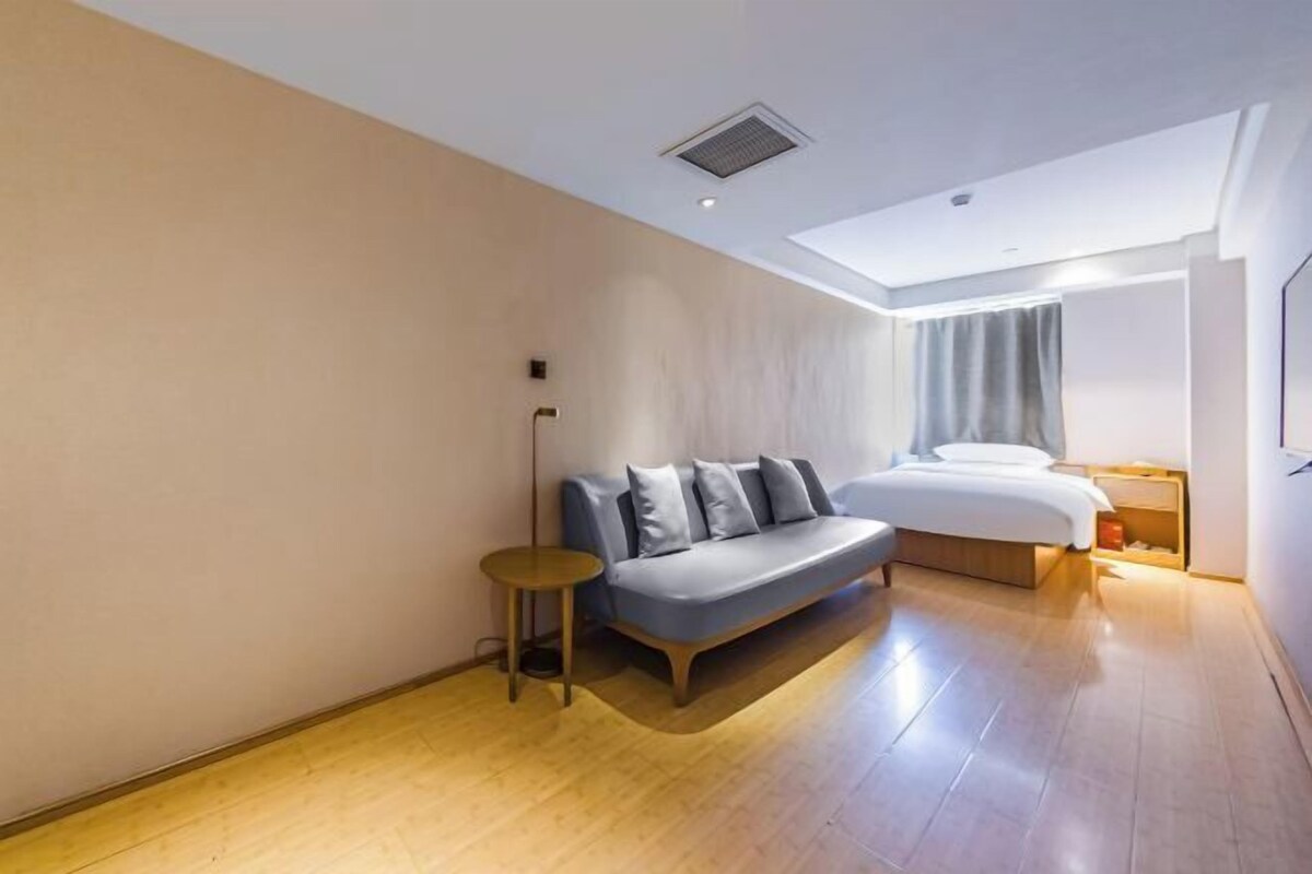 A modern hotel room with a sofa, a bed, a small round table, and a nightstand.