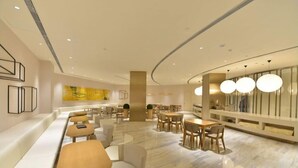 A modern hotel lobby with seating areas, a central pillar, and a wall with geometric decor. - Ji Hotel Beijing West Railway Station South Square (Beijing)