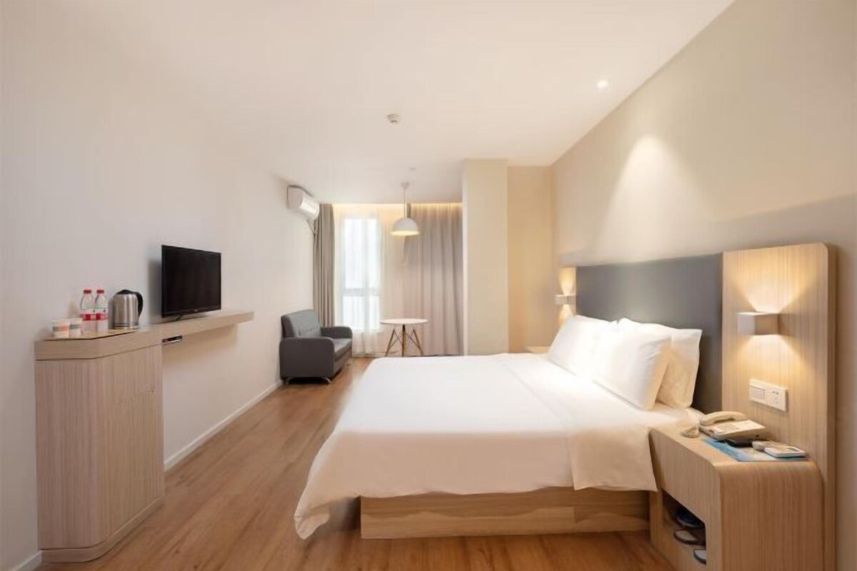 Een moderne hotelkamer met een groot bed, nachtkastje, televisie en een klein bureau.