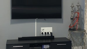 A flat-screen TV mounted on a wall, a black entertainment unit with a W-KING logo, and a hookah on a small table. - Stratford city apartment (London)