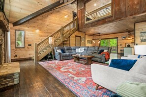 A spacious living room with a large sectional sofa, a coffee table, and a patterned rug. A staircase with wooden railings leads to an upper level.