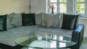 A modern living room with a sectional sofa, a glass coffee table, and a vase with flowers on a windowsill. - Amazing Apartment in Wernigerode With Wifi and 2 Bedrooms (Wernigerode)