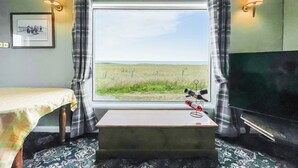 A room with a bed, a small table, a TV, and a window with a view of a field. - The view rivals anywhere, it’s amazing. (Reiss, near Wick)