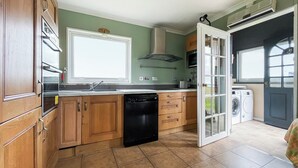 A kitchen with wooden cabinets, a dishwasher, a sink, and a window. - The view rivals anywhere, it’s amazing. (Reiss, near Wick)
