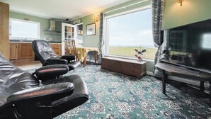 A living room with a television, leather chairs, a table, and a view of the outdoors. - The view rivals anywhere, it’s amazing. (Reiss, near Wick)