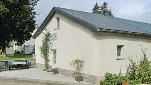 A single-story building with a sloped roof, a small porch with chairs, and potted plants. - Awesome Home in Hachiville With Wifi and 1 Bedrooms (Wincrange)