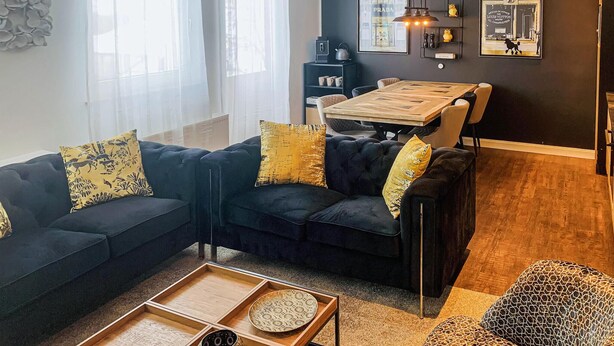 Una sala moderna con un sofá oscuro, una mesa de centro de madera y un comedor con mesa y sillas de madera.