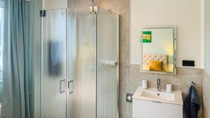 Un baño moderno con cabina de ducha de vidrio, un lavabo blanco con un espejo encima y una toalla colgada en la pared.